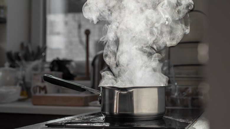 Ångande kastrull med kokande vatten på en spishäll i köket
